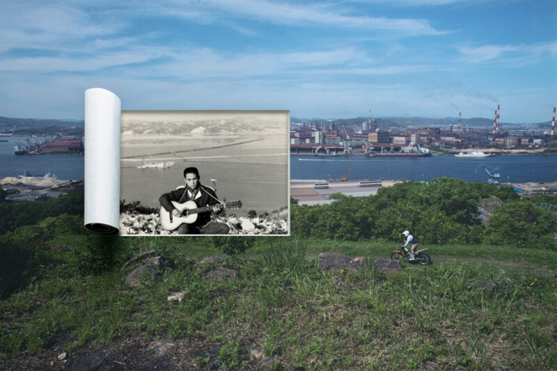 A black-and-white photo of a man playing guitar is superimposed on a grassy hillside, overlooking a cityscape with industrial buildings and water; a cyclist rides on the hill in the foreground under a blue sky.